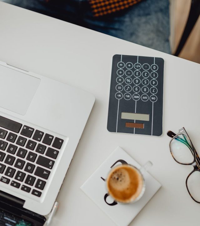 Overhead view of a sleek workspace featuring a laptop, a coffee cup, and a calculator.